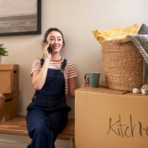 Woman talking on the phone while sitting on a bench with moving boxes nearby.